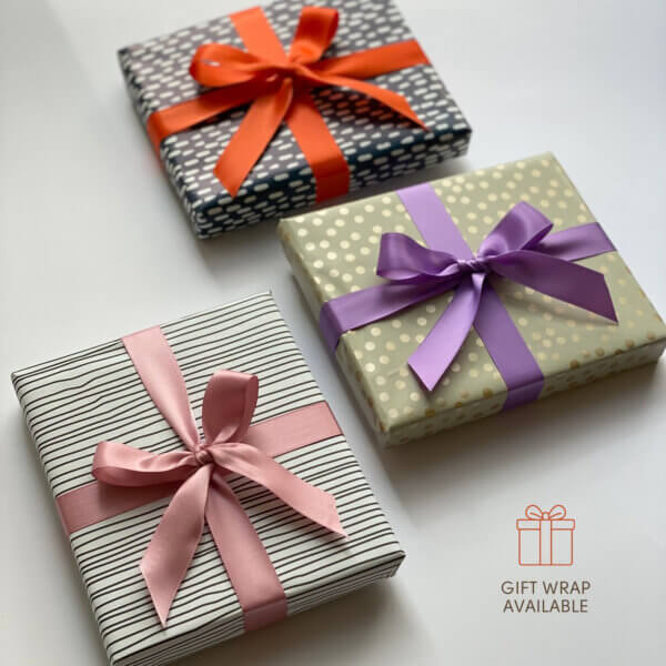 Gift wrapping option shown with three decorative wrapped boxes in black-and-white stripes, sage green dots and gray stripes, finished with orange, purple and pink ribbons.